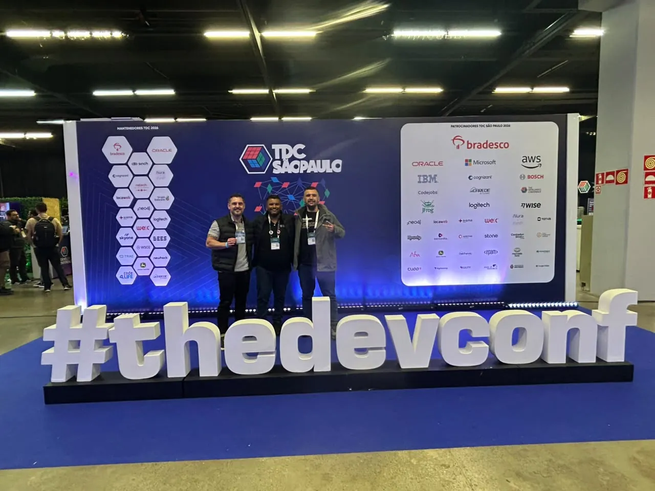 Três amigos diante do letreiro #thedevconf no TDC São Paulo 2026